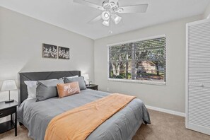 A bedroom with a bed, nightstands, a ceiling fan, a window with blinds, and a door.