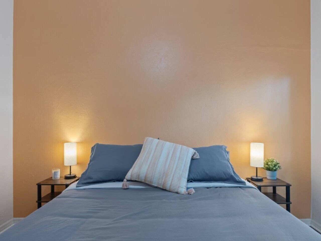 A bed with a blue mattress and pillows, two bedside tables with lamps, and a small potted plant on one table.