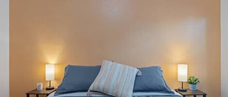 A bed with a blue mattress and pillows, two bedside tables with lamps, and a small potted plant on one table.