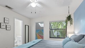 Een slaapkamer met een bed, een plafondventilator, een raam met uitzicht en een deur naar een badkamer.