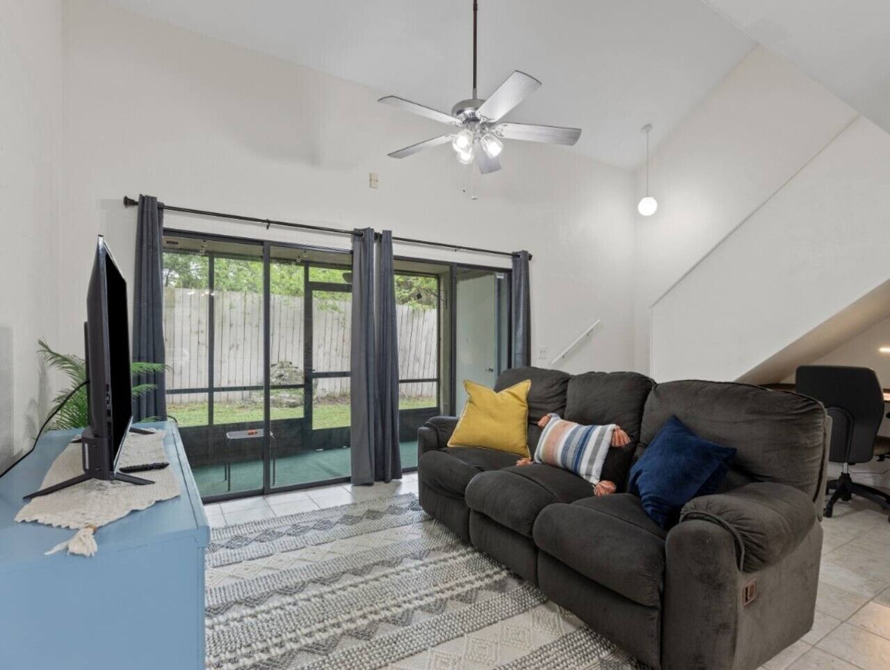 A living room with a sofa, a television, a ceiling fan, and a sliding glass door leading to a patio.