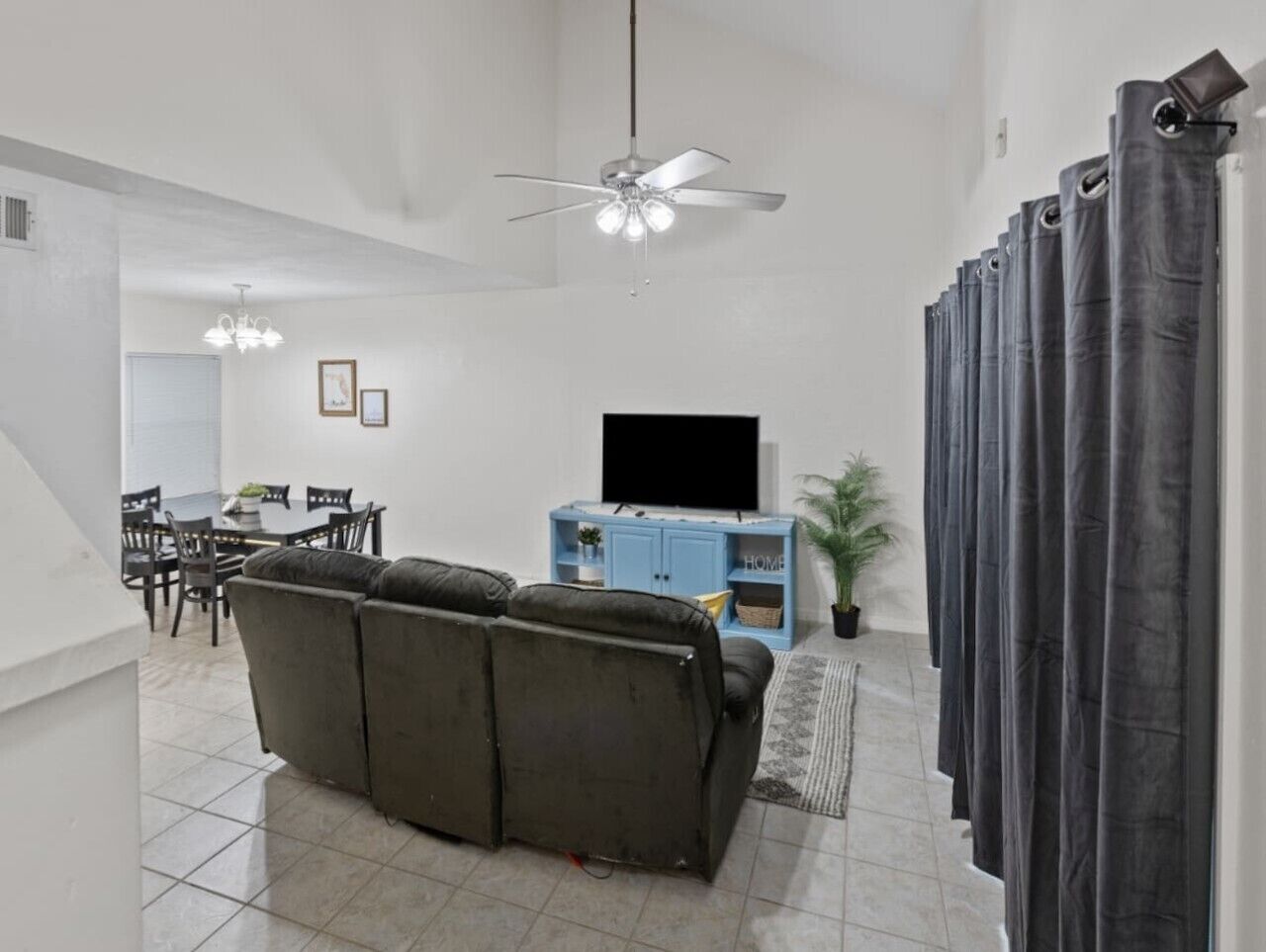 Un salon avec un canapé, un téléviseur, un ventilateur de plafond et des rideaux.