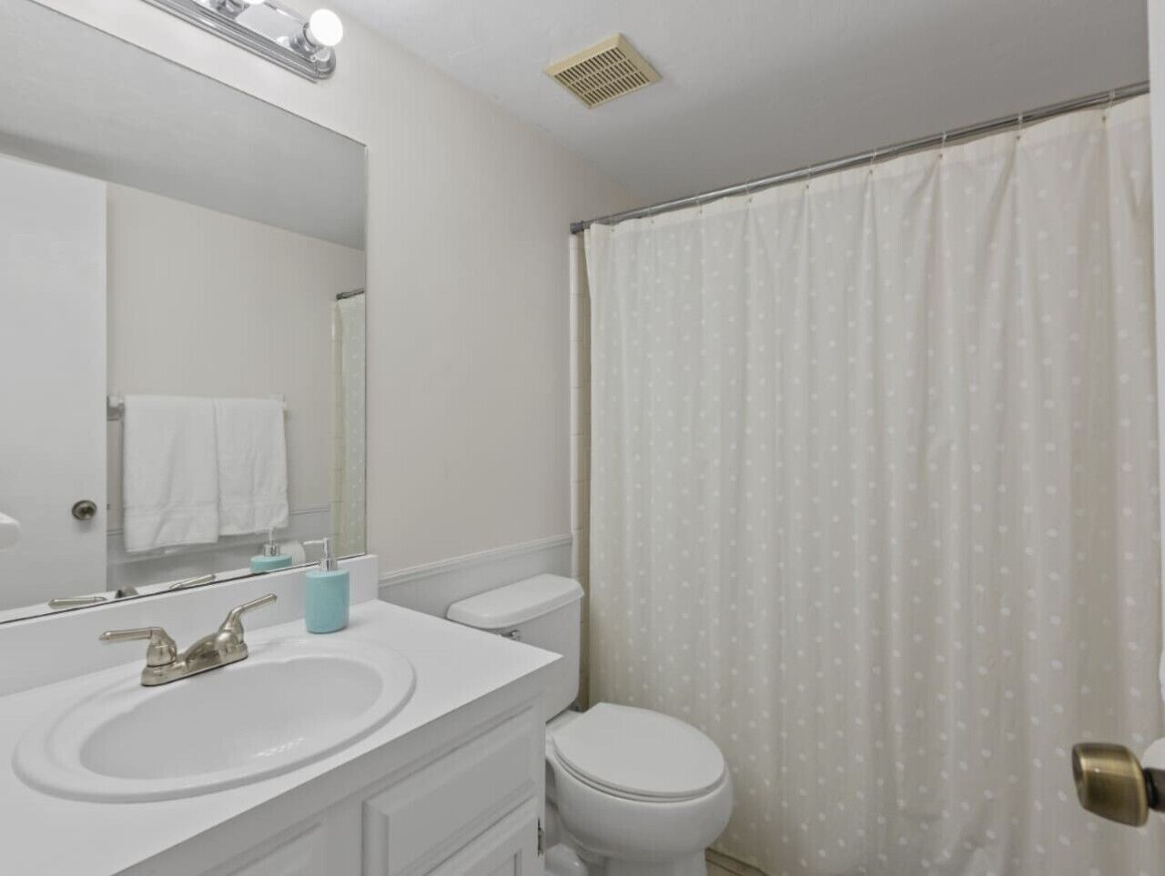Un bagno con lavandino bianco, specchio, water e tenda doccia.