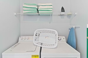 Uma área de lavanderia com toalhas empilhadas, um cesto e uma máquina de lavar roupa.