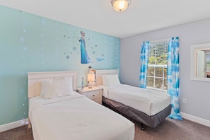 Quarto com duas camas, um mural na parede, uma janela com cortinas e uma mesa de cabeceira com abajur.