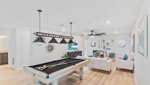 A modern living room with a pool table, a ceiling fan, and a large window. - 2021 Lelani Circle (Davenport)