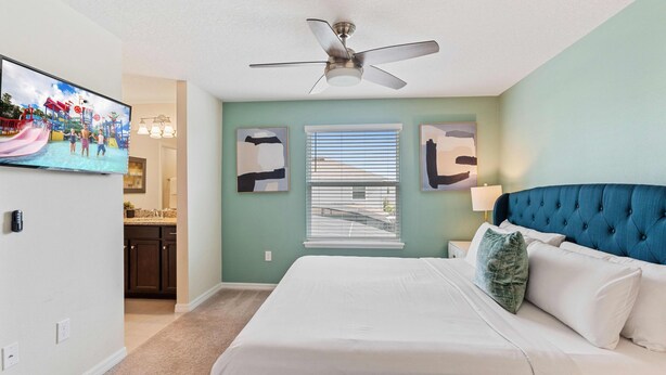 A bedroom with a bed, a ceiling fan, a TV, and a window with blinds. - 2021 Lelani Circle (Davenport)