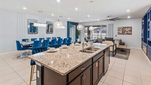 A modern kitchen with granite countertops, a central island, and blue chairs around a dining table. - 2021 Lelani Circle (Davenport)