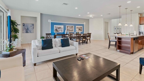 A modern living room with a white sofa, dark coffee table, and a dining area with a wooden table and chairs. - 8815 Macapa Drive (Kissimmee)