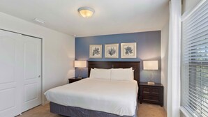 A bedroom with a large bed, two bedside tables, a ceiling light, and three framed pictures on the wall. - 8815 Macapa Drive (Kissimmee)