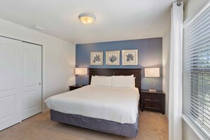 A bedroom with a bed, two bedside tables, a nightstand, a door, and a window with blinds. - 8815 Macapa Drive (Kissimmee)