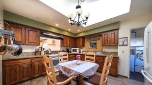 A kitchen with wooden cabinets, a dining table with chairs, a chandelier, and a view of the outside. - Starfish -Trinidad Ocean Ave - Couples Haven (Trinidad)
