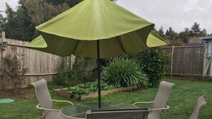 A patio with a round table and four chairs, an umbrella, and a wooden fence in the background. - Starfish -Trinidad Ocean Ave - Couples Haven (Trinidad)