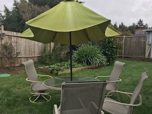 A patio with a round table and four chairs, an umbrella, and a wooden fence in the background.