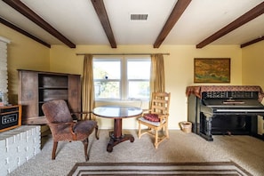 A living room with a piano, two chairs, a table, a fireplace, and a window with curtains.