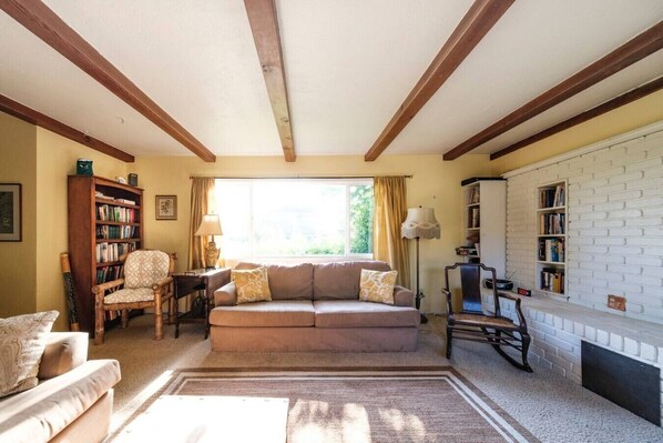 A living room with a sofa, armchairs, a bookshelf, a fireplace, and a window with curtains.
