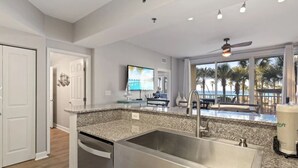 A kitchen with a large island, stainless steel sink, and a view of the pool and palm trees.