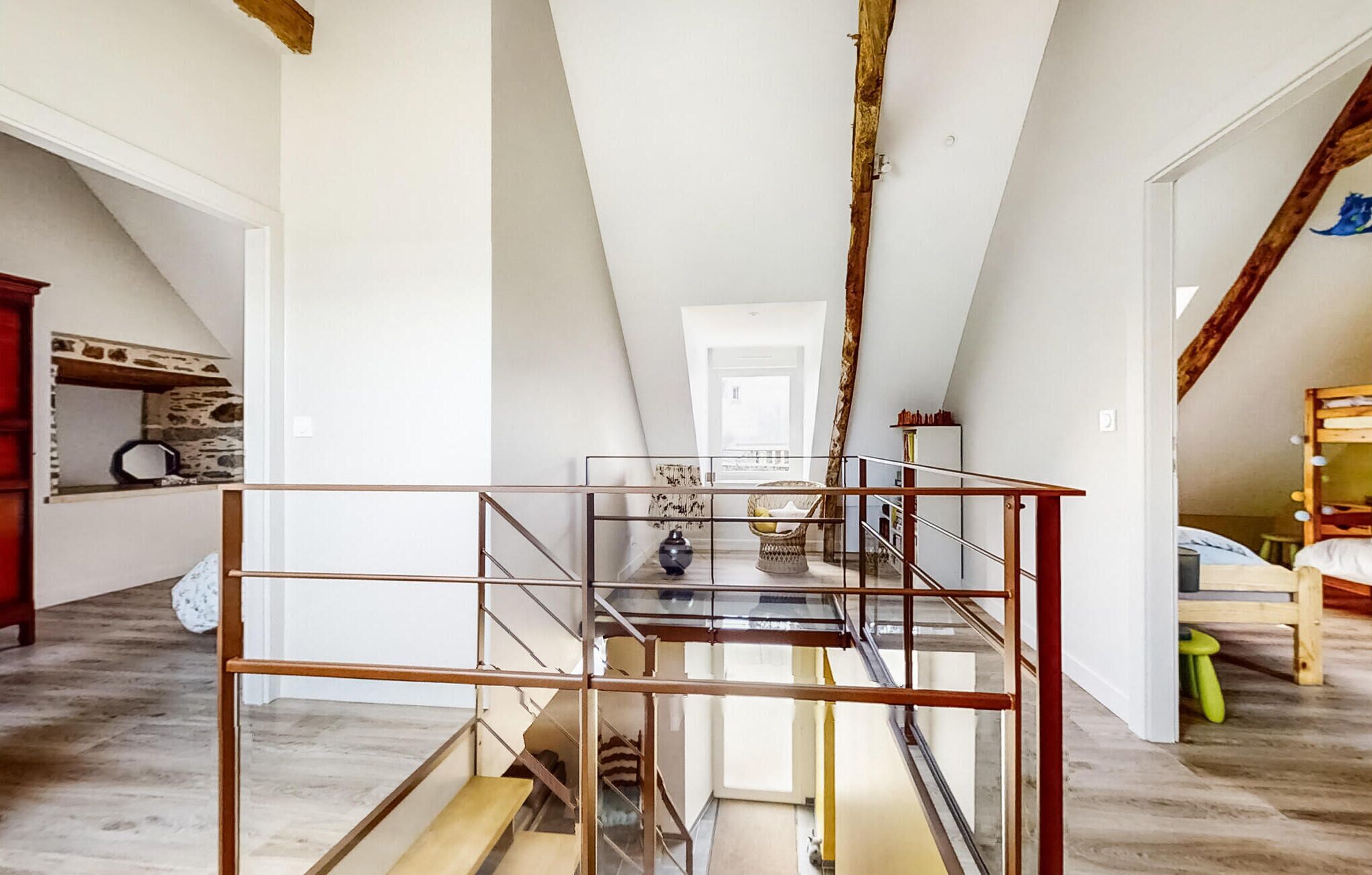 Un ático amplio con una escalera de cristal, vigas de madera y vistas a la habitación contigua.
