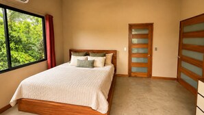 A bedroom with a bed, a ceiling fan, an air conditioning unit, a window with curtains, and a door with frosted glass panels. - Modern villa with stunning jungle views (Provincia de Puntarenas)