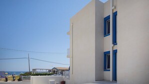 A building with a white facade and blue window frames, located near a beach with umbrellas and a few parked vehicles.