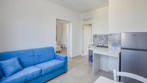A compact living space with a blue sofa, a kitchenette with a refrigerator, and a tiled backsplash.