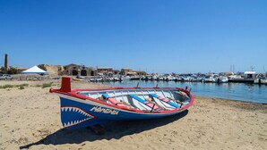 A beach with a rowboat, a tent, and a marina in the background.