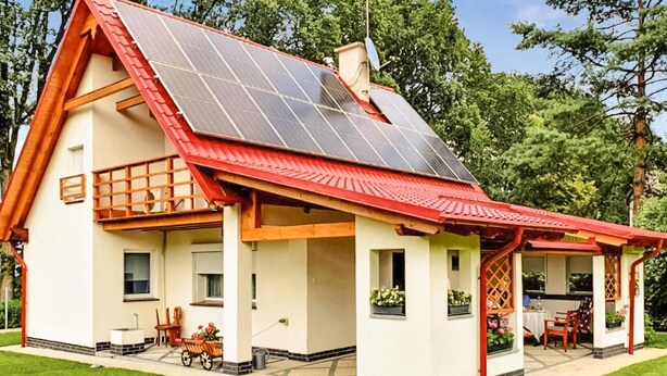 Une maison avec un toit rouge, des panneaux solaires et une véranda couverte aménagée avec du mobilier d’extérieur.