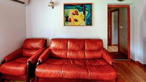 Un canapé en cuir rouge dans un salon, avec un tableau accroché au mur et une porte visible au fond.
