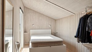 Un dormitorio con una cama, una silla, perchero y techo de madera.