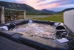 A hot tub with a wooden deck and a scenic mountain view.