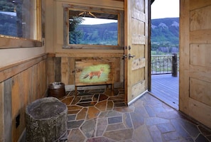 A wooden interior with a stone floor, a painting of a fox, and a view of mountains through a window.