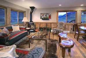 A cozy living room with a fireplace, a sofa, a coffee table, and a view of mountains through large windows.