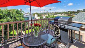 Un balcone con un ombrellone rosso, un barbecue e un tavolo con sedie.