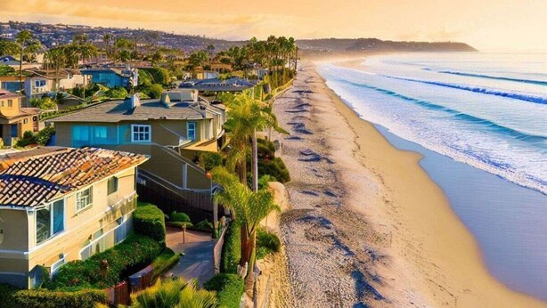 Una zona residenziale lungo la costa, con case affacciate sulla spiaggia, cielo sereno e onde oceaniche.