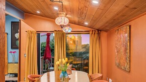 Zona pranzo con tavolo in legno, sedie, un vaso con fiori, un lampadario e vista attraverso una porta vetrata.