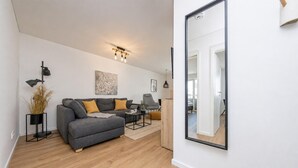 A modern living room with a grey sofa, a coffee table, and a large mirror. - Ferienwohnung Meerzeit (Kappeln)