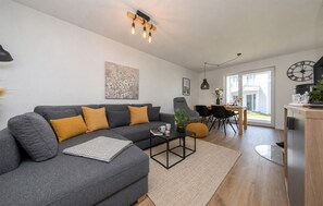 A modern living room with a grey sofa, a coffee table, and a dining area with chairs and a table.