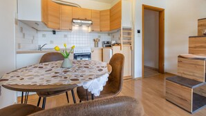 A modern kitchen with wooden cabinets, a dining table with a lace tablecloth, and a vase with flowers.
