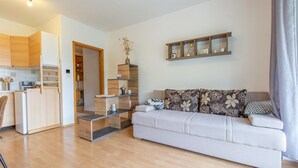 A modern living room with a sofa, a coffee table, and a kitchen area with wooden cabinets and a refrigerator.