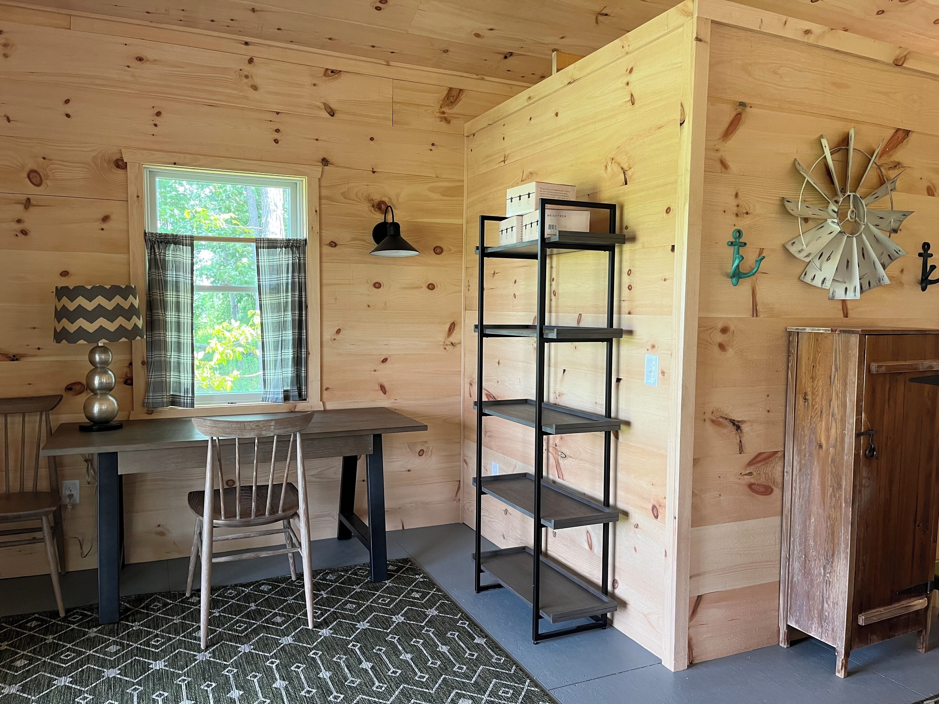 A wooden cabin interior with a desk, chair, shelves, and a decorative windmill.