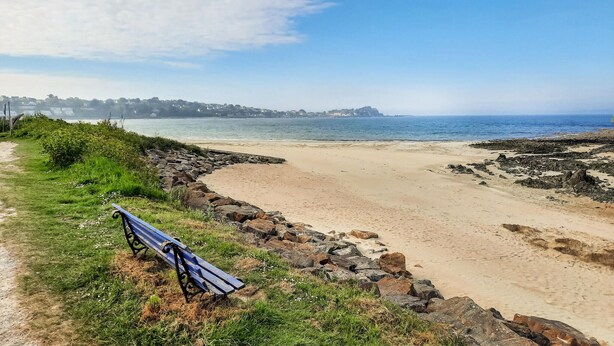 Une plage avec un banc, un rivage rocheux et une vue dégagée sur l’océan.