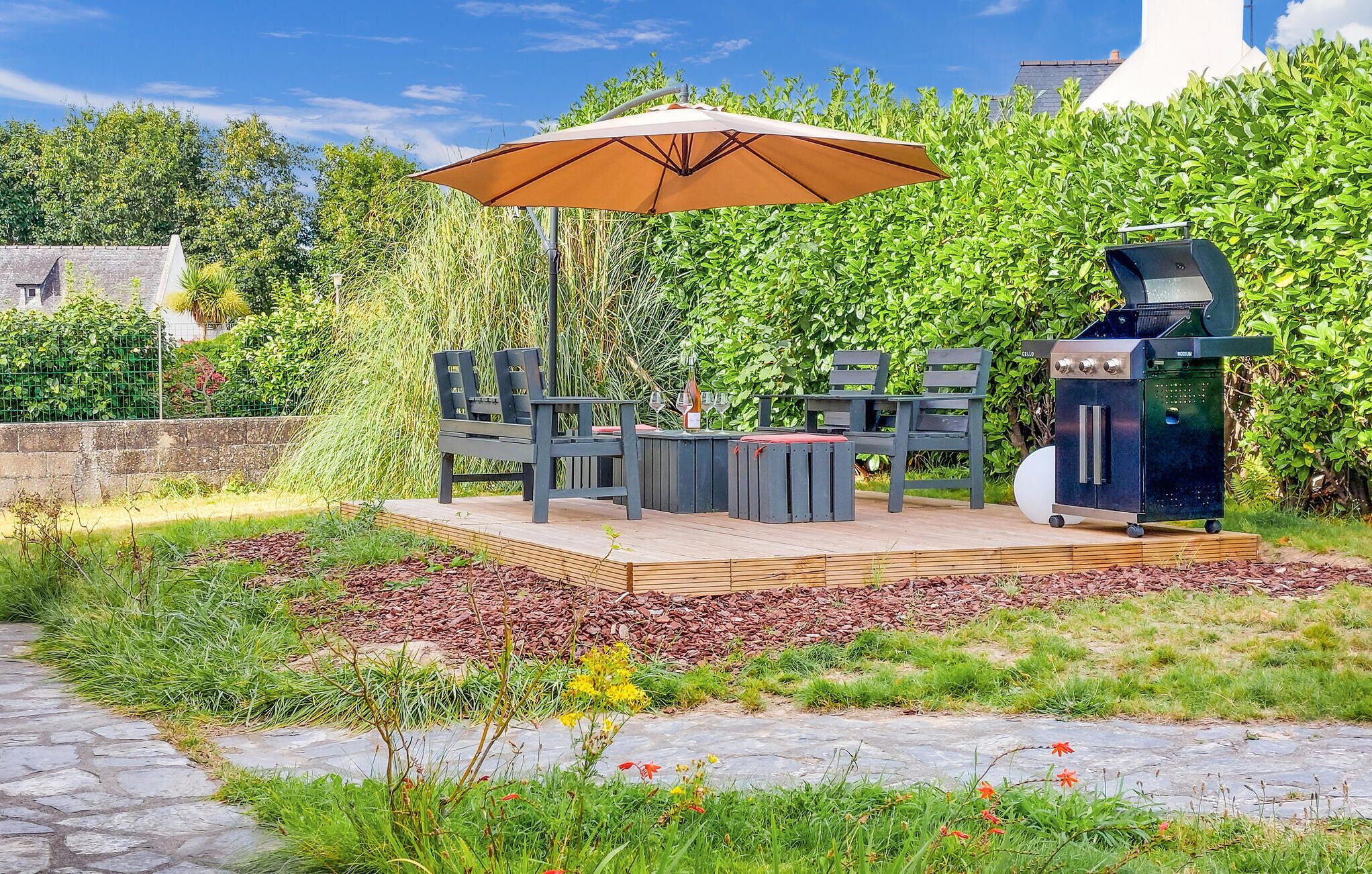 An outdoor patio with a grill, seating, and a large umbrella.