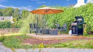 Une terrasse extérieure équipée d’un barbecue, de sièges et d’un grand parasol.