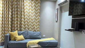 Una sala de estar moderna con un sofá gris, cojines amarillos, un reposapiés negro y un televisor montado en la pared.
