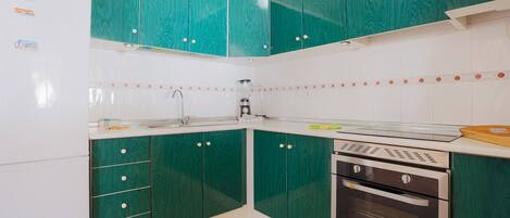 Una cocina con gabinetes color turquesa, un refrigerador blanco, un lavamanos y un horno doble.