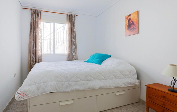 A bedroom with a bed, a window with curtains, a bedside table with a lamp, and a painting on the wall. - Stunning home in Los Alcázares with WiFi (Los Alcázares)