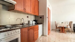 A kitchen with wooden cabinets, a gas stove, a coffee maker, and a dining area with a table and chairs.