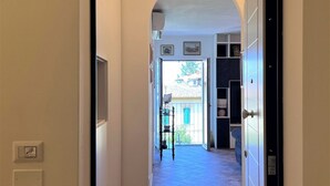 Un couloir avec une porte en arc donnant sur un balcon. On y trouve des interrupteurs d’éclairage fixés au mur et une petite étagère sur laquelle est posée une plante en pot.