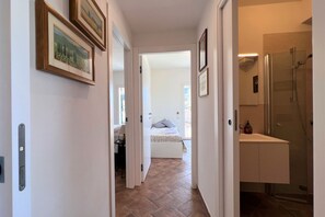 Un passadís amb quadres a la paret que condueix a un dormitori amb llit i un bany amb dutxa.