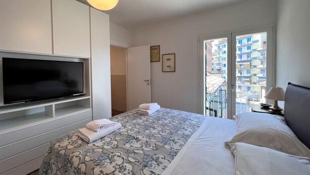 Une chambre d’hôtel dotée d’un grand lit, d’une télévision à écran plat, d’un balcon offrant une vue sur les bâtiments et d’une porte donnant accès à la salle de bain.